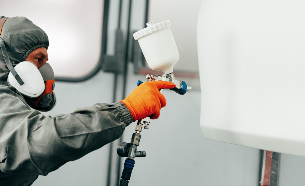 Applying Protective Coating Using a Spray Gun and Industrial Pump System Technician applying protective coating with a spray gun connected to an industrial pump system